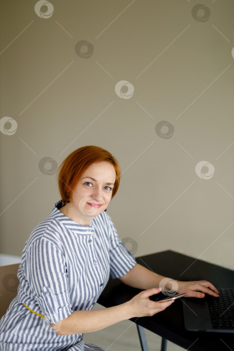 Скачать женщина сидит на фоне бежевой стены, работает за ноутбуком фотосток Ozero