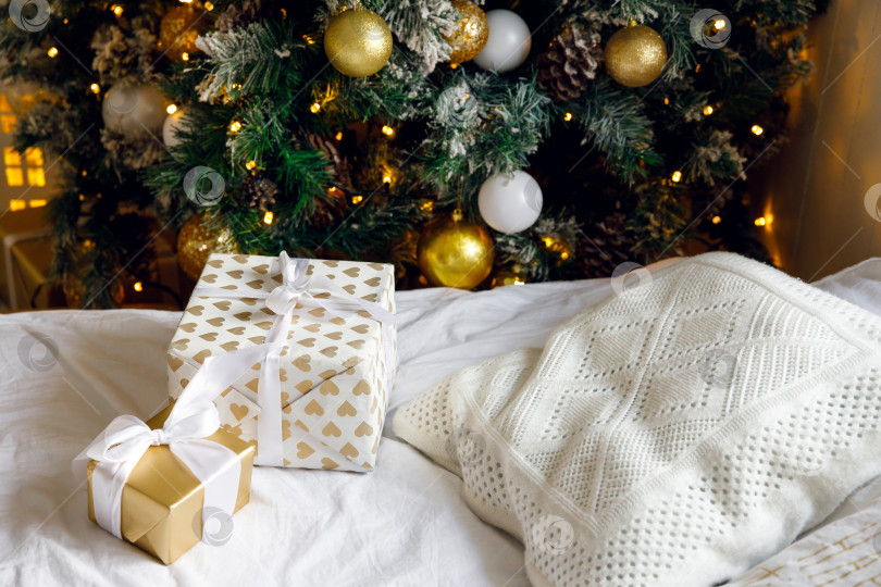 Скачать подарки на кровати на белой простыне, рядом с украшенной рождественской елкой фотосток Ozero