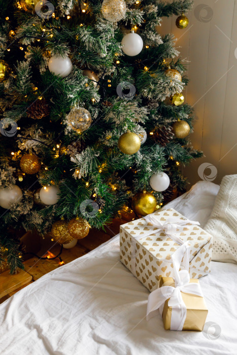 Скачать Рождественские подарки на кровати на белой простыне, рядом с украшенной рождественской елкой фотосток Ozero