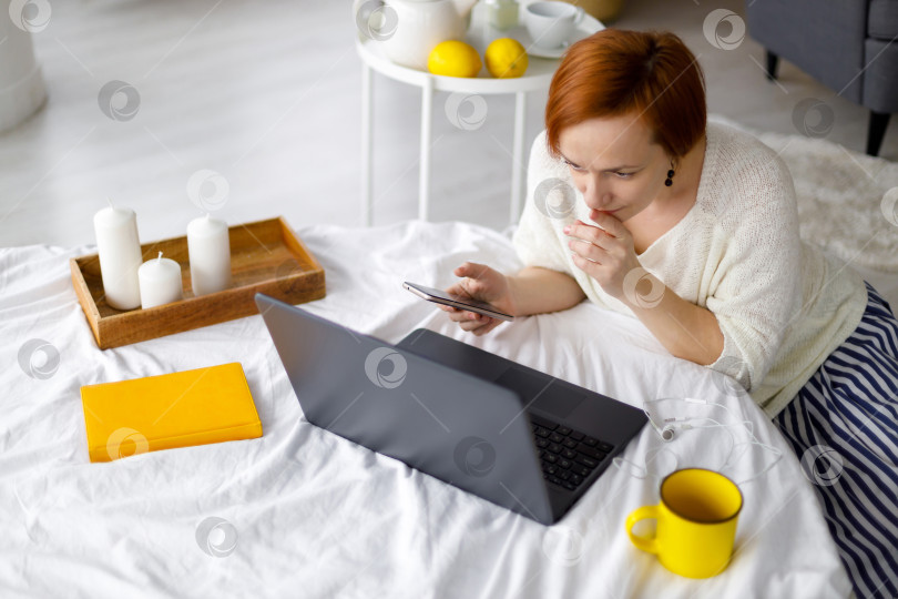 Скачать женщина в свитере работает на кровати с ноутбуком фотосток Ozero
