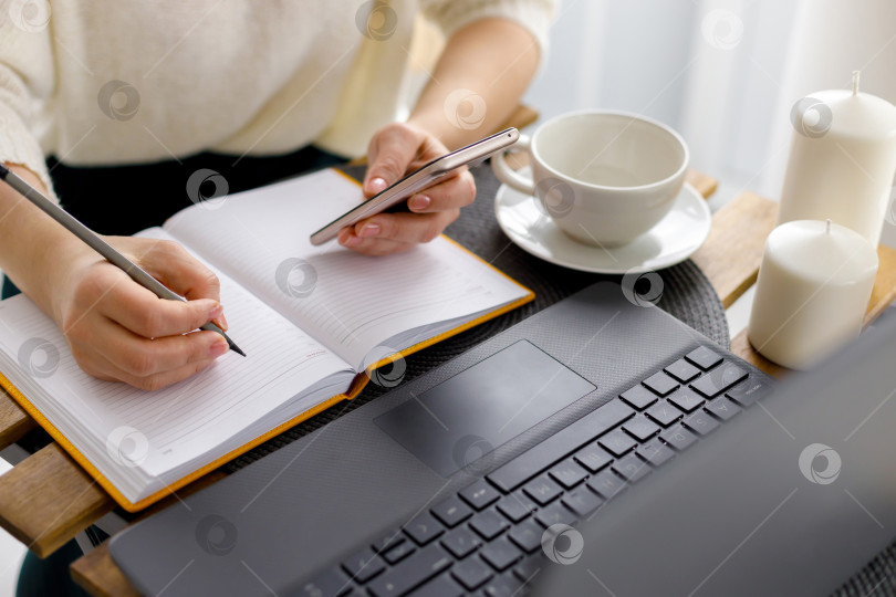 Скачать деловая женщина работает за ноутбуком, держа в руке смартфон фотосток Ozero