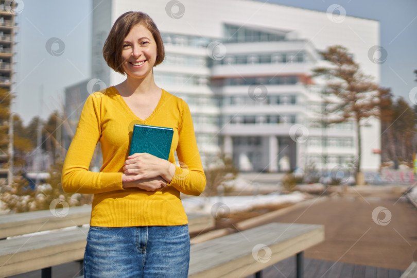 Скачать портрет улыбающейся студентки в желтом свитере с книгой в руках фотосток Ozero