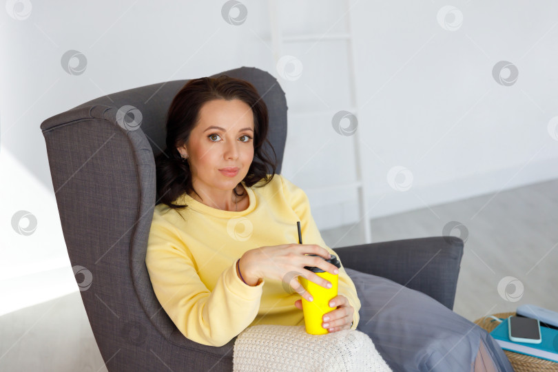 Скачать женщина в толстовке сидит на стуле, держит в руках бумажный стаканчик фотосток Ozero