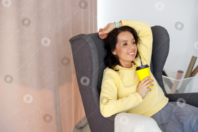 Скачать женщина в толстовке сидит на стуле, держит в руках бумажный стаканчик фотосток Ozero