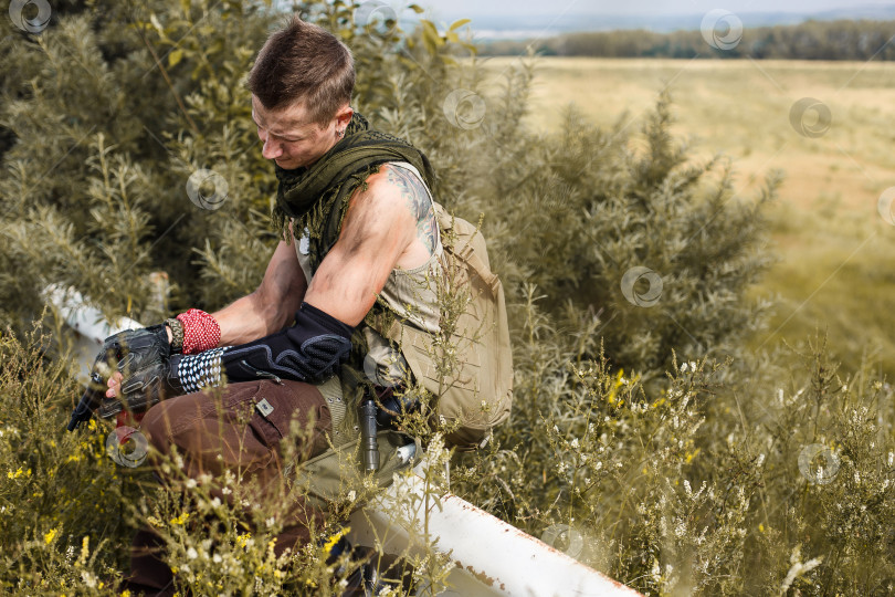 Скачать мужчина-вандал в грязной одежде и с пистолетом сидит на заборе фотосток Ozero
