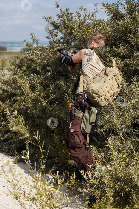 Скачать мужчина в грязной одежде прячется в кустах и стреляет из пистолета фотосток Ozero