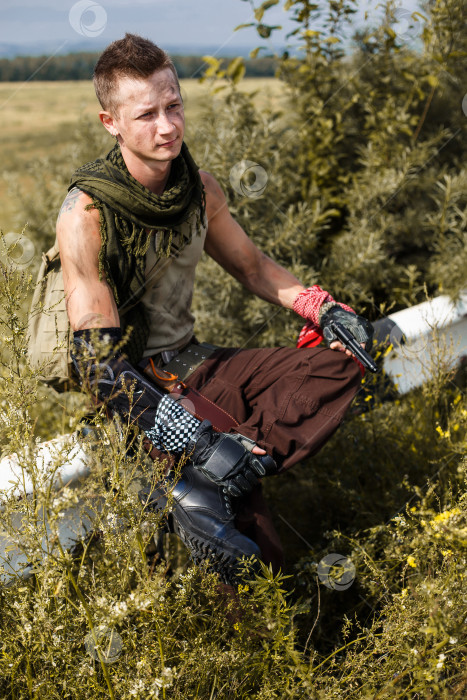 Скачать мужчина-вандал в грязной одежде и с пистолетом сидит на заборе фотосток Ozero