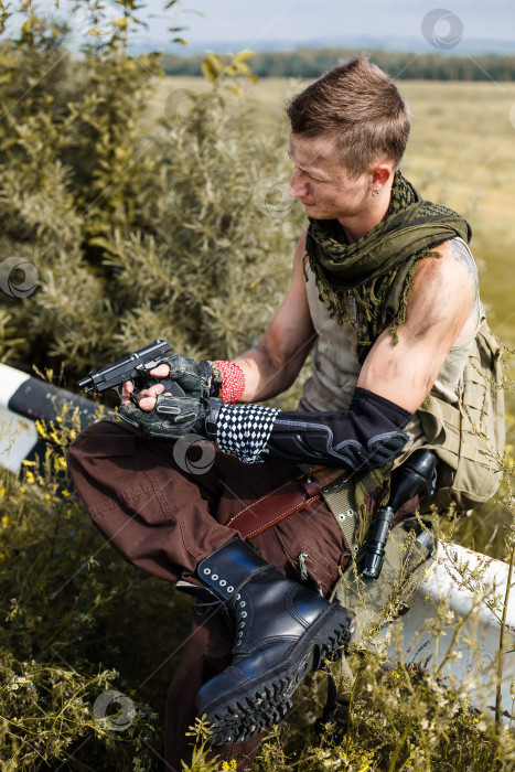 Скачать мужчина-вандал в грязной одежде и с пистолетом сидит на заборе фотосток Ozero