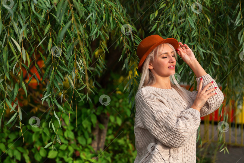 Скачать женщина в свитере стоит под ветвями и зелеными листьями фотосток Ozero