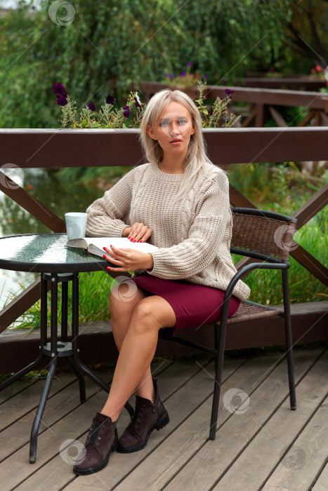 Скачать блондинка в свитере сидит за столом и читает книгу фотосток Ozero