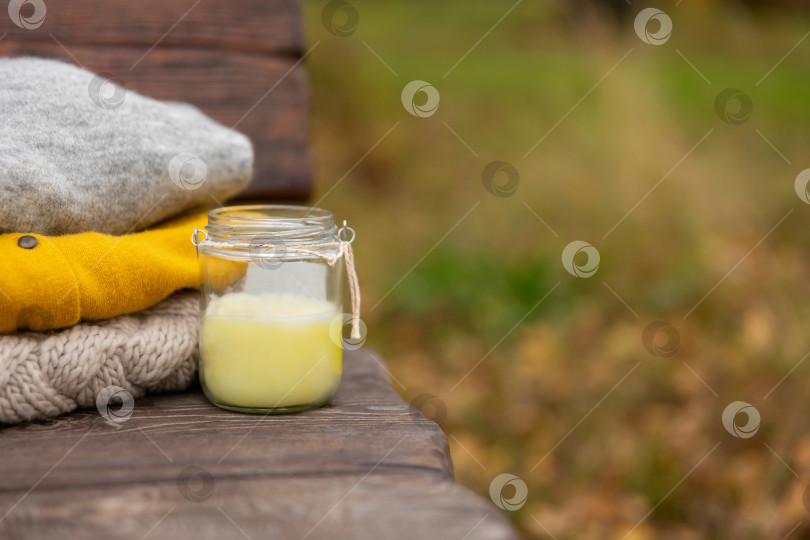 Скачать вязаная одежда и свеча в банке на деревянной скамейке в парке. Осенний теплый шерстяной свитер фотосток Ozero