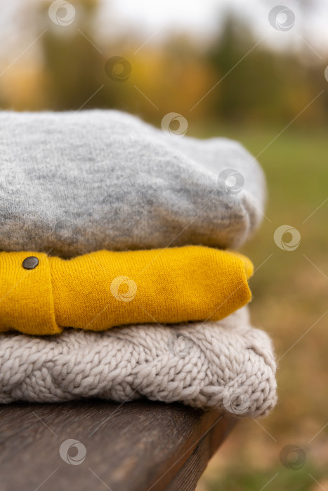 Скачать стопка вязаной одежды на деревянной скамейке в парке. Осенний теплый шерстяной свитер фотосток Ozero