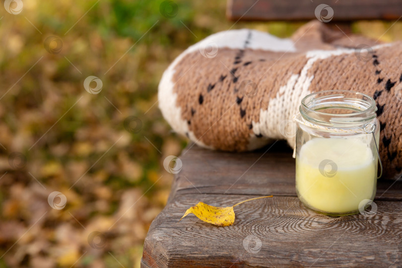 Скачать вязаная одежда и свеча в банке на деревянной скамейке в парке. Осенний теплый шерстяной свитер фотосток Ozero