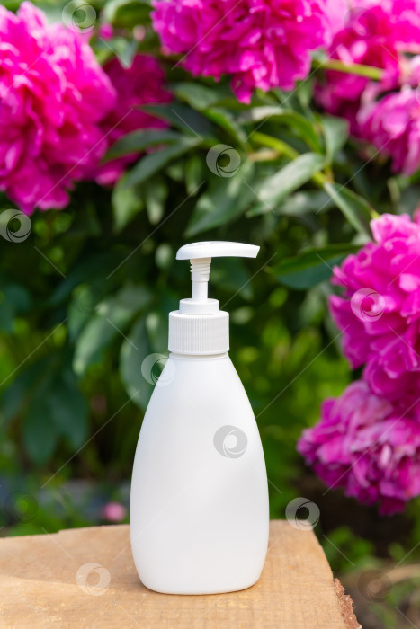 Скачать белая косметическая бутылочка для мыла или шампуня на деревянной полке на фоне пионов. Для демонстрации вашего продукта фотосток Ozero