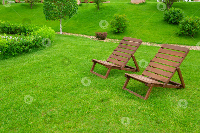 Скачать Реклама для отдыха и туризма. Два пустых коричневых деревянных шезлонга на зеленой траве свежего газона. фотосток Ozero