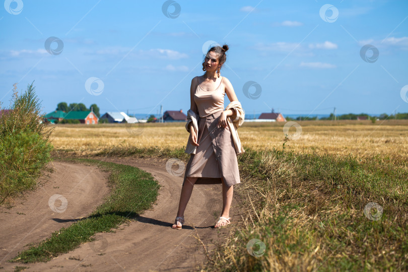 Скачать Молодая красивая брюнетка-модель в бежевом платье позирует на фоне скошенного пшеничного поля фотосток Ozero