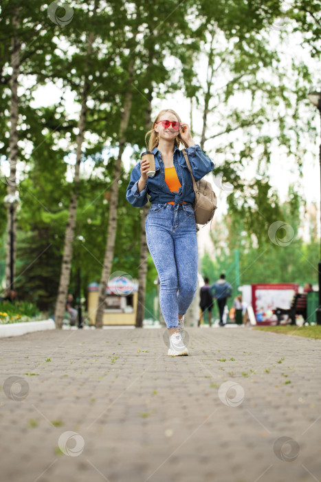 Скачать Молодая блондинка в синих джинсах прогуливается по летнему парку фотосток Ozero