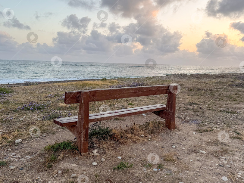 Скачать Умиротворяющий вид на пляж С деревенской скамейкой, откуда открывается вид на Пологие волны и красочное Закатное небо. фотосток Ozero