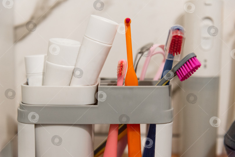 Скачать Зубные щетки и зубные пасты для полости рта в пластиковом контейнере на полке в ванной комнате фотосток Ozero