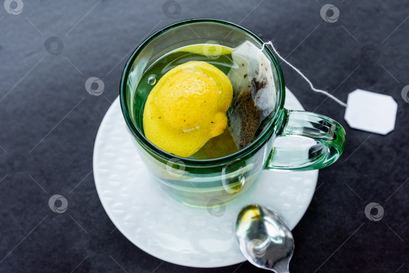 Скачать Упакованный черный полезный травяной чайный напиток с лимонной заваркой в стеклянной кружке на столе фотосток Ozero