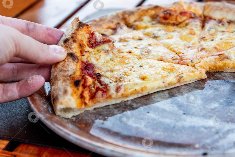 Скачать Посетитель ресторана-пиццерии держит в руке кусочек итальянской пиццы "Маргарита" фотосток Ozero