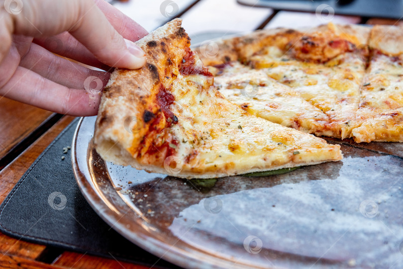Скачать Посетитель ресторана-пиццерии держит в руке кусочек итальянской пиццы "Маргарита" фотосток Ozero