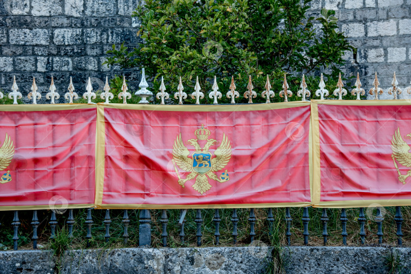 Скачать Национальный флаг независимого государства Черногория висит на флагштоке на фоне металлического забора фотосток Ozero