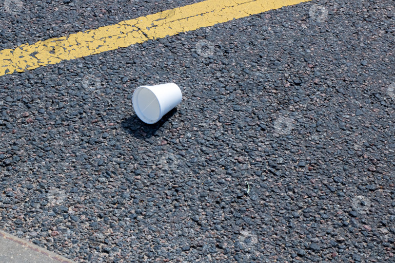 Скачать Одноразовый стаканчик, небрежно брошенный на асфальтовую дорожку фотосток Ozero