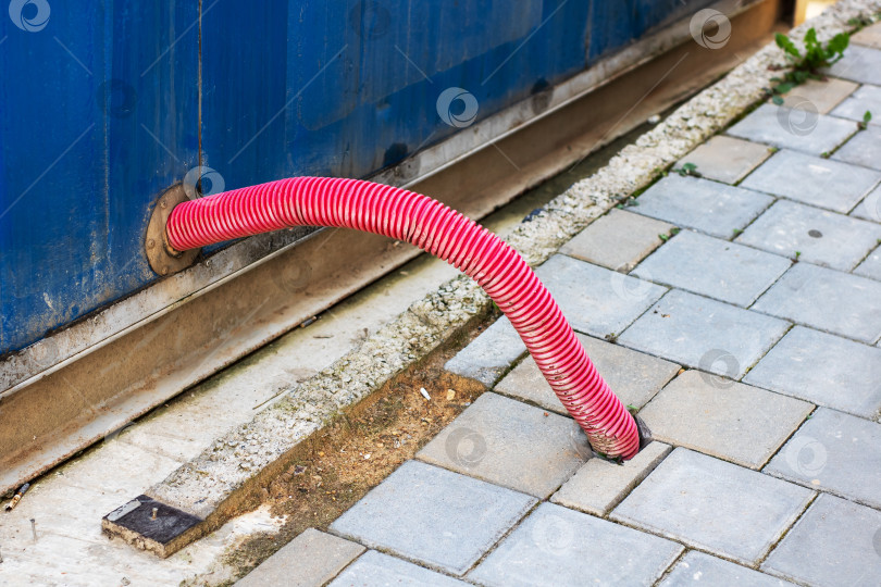 Скачать Ярко-красный шланг выходит из контейнера на асфальтированную площадку фотосток Ozero