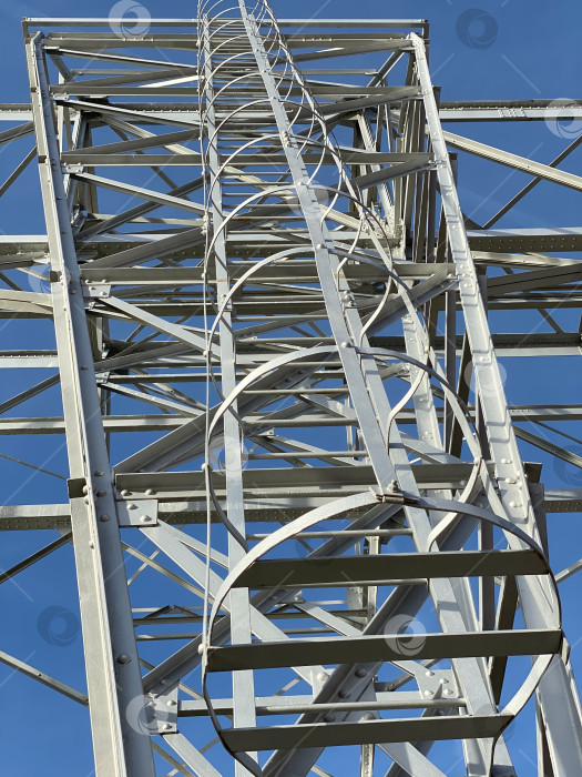 Скачать Башня электропередачи с детализированной металлической конструкцией и лестницей на фоне ясного голубого неба фотосток Ozero