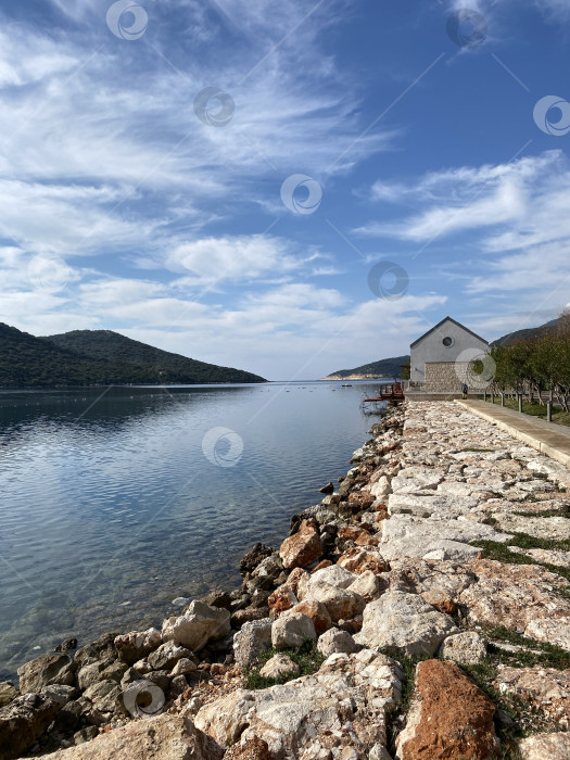 Скачать Прибрежный каменный дом, отражающийся в спокойной воде на фоне облачного неба и изрезанной тропинки, ведущей к горизонту фотосток Ozero