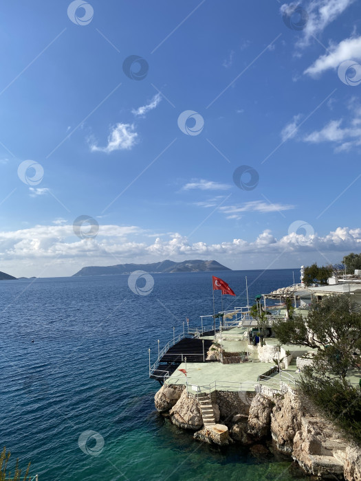 Скачать Турецкий флаг развевается на побережье с чистым небом и синим морем, запечатлевая спокойную сцену отдыха фотосток Ozero