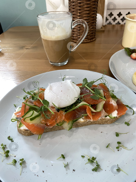 Скачать Копченый лосось и яйцо-пашот на тосте с овощами и латте на деревянном столе в кафе фотосток Ozero