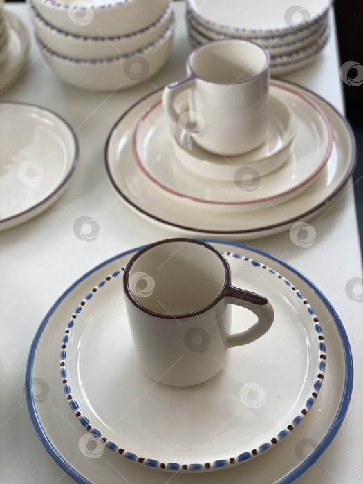 Скачать Керамические тарелки и кружки, расставленные на белом столе в качестве декоративного кухонного фона фотосток Ozero