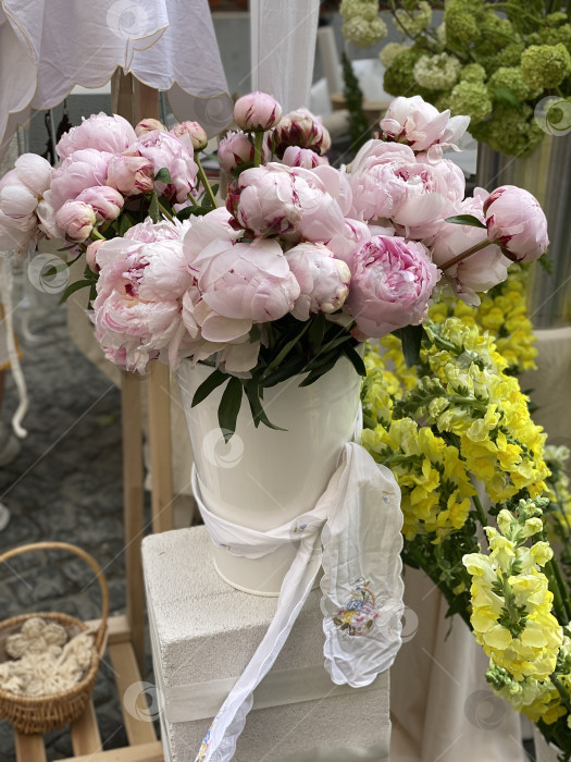 Скачать Букет розовых пионов в белой вазе в окружении желтых цветов на уличном рынке фотосток Ozero