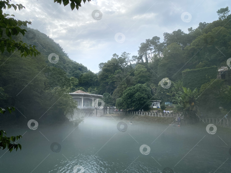 Скачать Туманный вид на озеро с пышными зелеными деревьями и старым строением на фоне безмятежного природного ландшафта фотосток Ozero