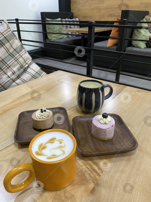 Скачать Кофе и десерты на деревянном столе в уютной обстановке кафе с креслами на заднем плане фотосток Ozero
