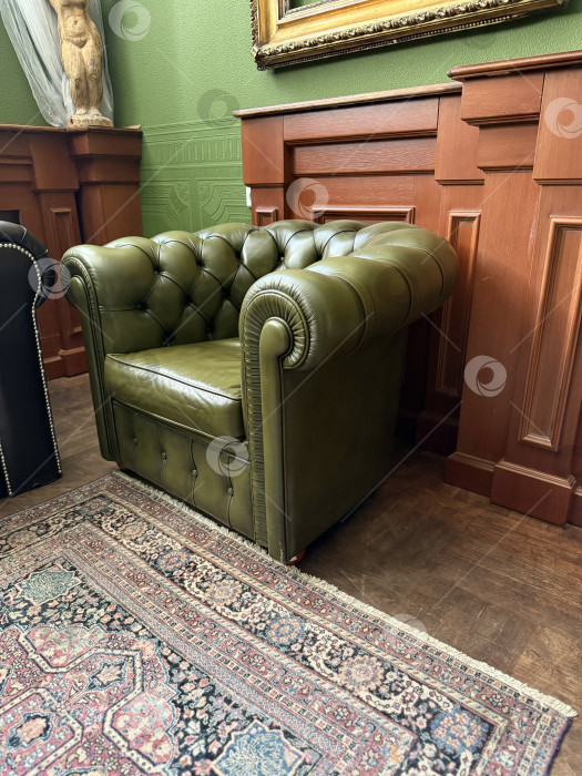 Скачать Роскошное зеленое кожаное кресло в винтажной комнате с богато украшенными деревянными панелями и ковром на заднем плане фотосток Ozero