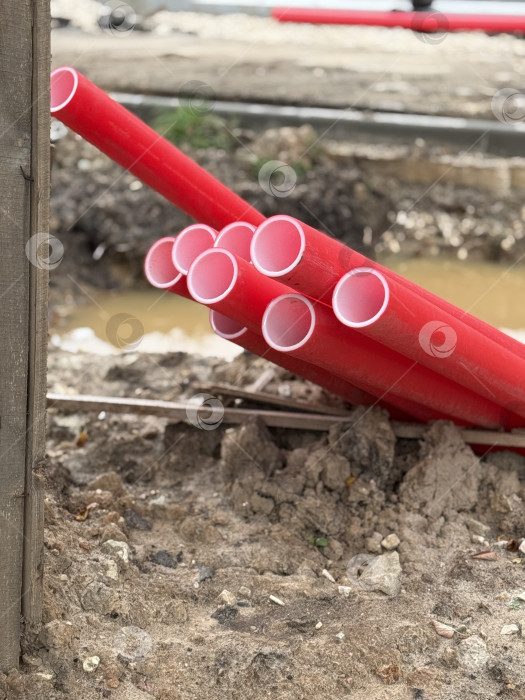 Скачать Красные пластиковые строительные трубы, уложенные штабелями на грязном участке, демонстрируют промышленные строительные материалы фотосток Ozero