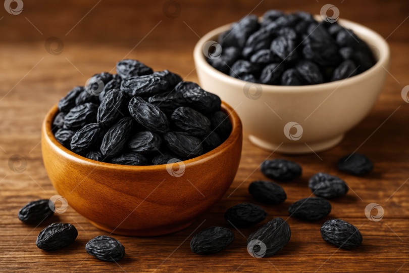 Скачать Крупный план черных сухофруктов в деревянных и керамических вазах на деревенском столе, демонстрирующих их сочную текстуру и насыщенный цвет. фотосток Ozero