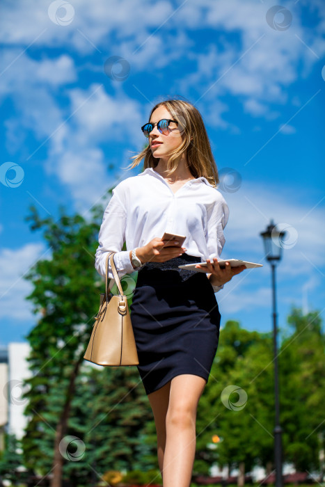 Скачать Молодая ассистентка в белой блузке звонит по телефону на улице фотосток Ozero