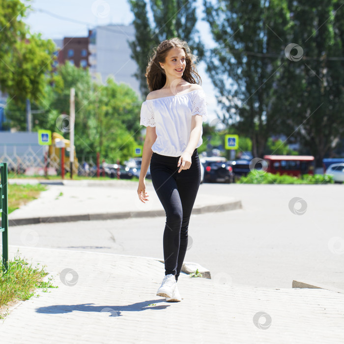 Скачать Молодая красивая брюнетка в джинсах и белой блузке прогуливается по летней улице фотосток Ozero