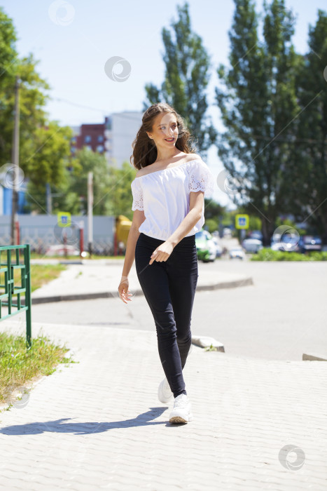 Скачать Молодая красивая брюнетка в джинсах и белой блузке прогуливается по летней улице фотосток Ozero