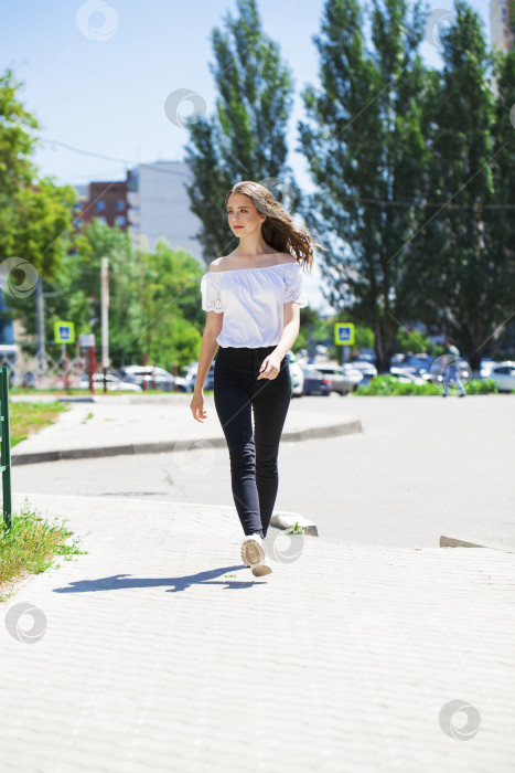 Скачать Молодая красивая брюнетка в джинсах и белой блузке прогуливается по летней улице фотосток Ozero