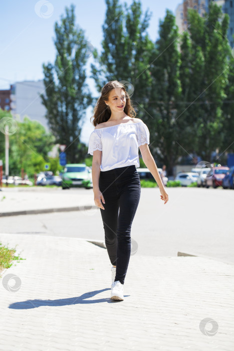 Скачать Молодая красивая брюнетка в джинсах и белой блузке прогуливается по летней улице фотосток Ozero