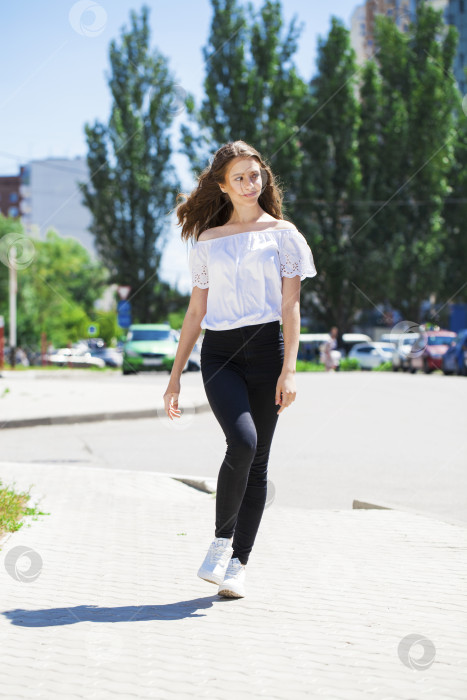 Скачать Молодая красивая брюнетка в джинсах и белой блузке прогуливается по летней улице фотосток Ozero