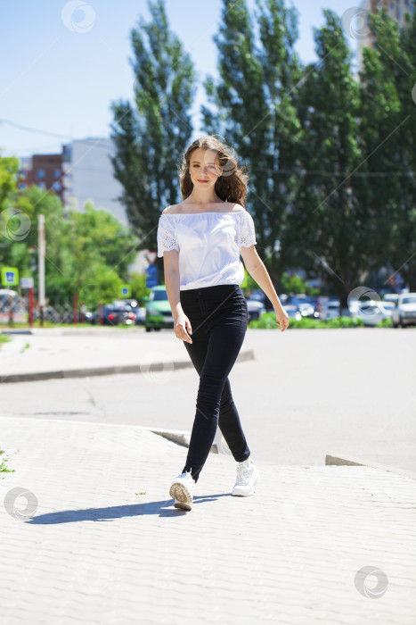 Скачать Молодая красивая брюнетка в джинсах и белой блузке прогуливается по летней улице фотосток Ozero