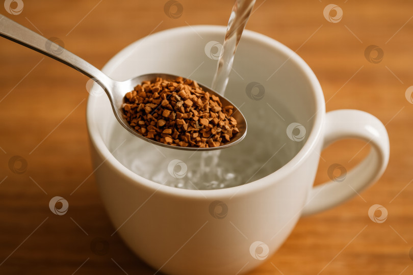 Скачать Идеальный момент: Насыпьте гущу растворимого кофе в белую кружку с горячей водой, чтобы быстро и вкусно приготовить напиток. фотосток Ozero