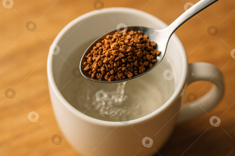 Скачать Размешивание зерен растворимого кофе в теплой воде позволяет быстро заварить его и насладиться ароматом в белой кружке на деревянном фоне. фотосток Ozero