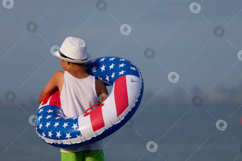 Скачать Ребенок наслаждается игрой на пляже с надувным кольцом в цветах американского флага в солнечный день фотосток Ozero
